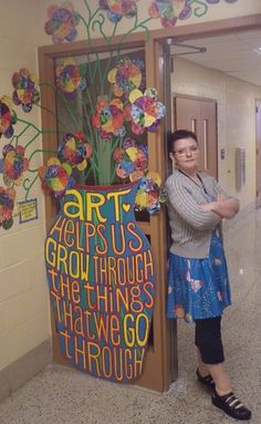 a woman standing next to a sign with flowers on it in an empty hallway area