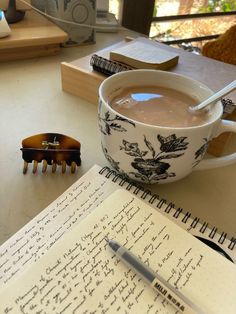 a cup of coffee sitting on top of a table next to an open notepad