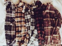 three flannel shirts laid out on top of a white sheet with one laying down