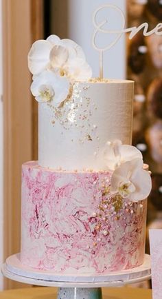 a three tiered cake with white and pink flowers on the top is sitting on a table