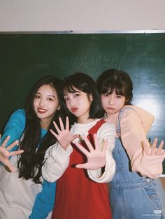 three girls posing for the camera in front of a chalkboard with their hands up