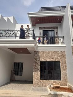 two people are standing on the balcony of a house that is being built with stone and stucco