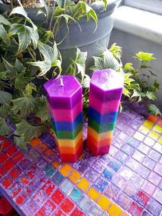 two colorful candles sitting on top of a table next to a potted green plant