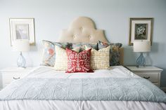 a white bed topped with lots of pillows next to two framed pictures on the wall