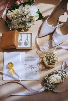 the wedding stationery is laid out on the bed with flowers and jewelry, such as bride's shoes