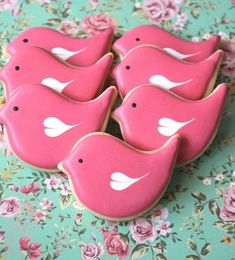 pink decorated cookies sitting on top of a green floral tablecloth with white birds painted on them