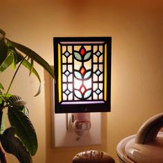 a stained glass window is mounted on the wall next to a potted green plant