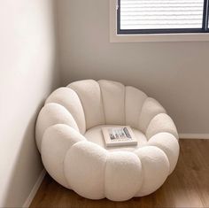 a white chair sitting in front of a window next to a book on top of a wooden floor