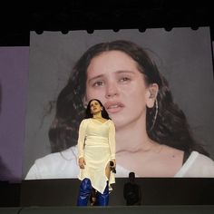 a woman standing on stage in front of a large screen with an image of a woman