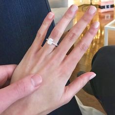 a woman's hand holding an engagement ring in the middle of her left hand