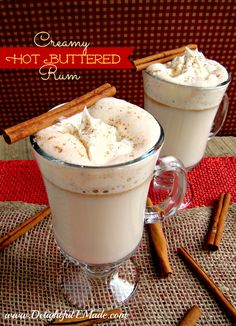 two glasses of hot chocolate with whipped cream and cinnamon sticks on the table next to them