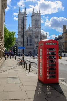 a red phone booth sitting on the side of a road next to a tall building