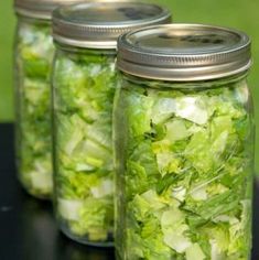 three mason jars filled with lettuce sitting on top of a black table next to each other