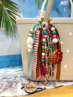 Elevate your beach or poolside style with the  Beach Bogg Bag Charm. This charming accessory adds a touch of summer flair to your favorite bag, making it perfect for sunny days by the water. The playful design of the charm embodies the carefree spirit of the season, while the vibrant colors capture the essence of summertime. With its whimsical appeal, this bag charm is sure to become a fun and eye-catching addition to your accessory collection. The tassel detail adds a trendy touch, ensuring that you stand out with a unique and stylish statement wherever you go. Bring a bit of beachside relaxation and poolside vibes to your look with this must-have summer bag charm. All of our key chains and/or charms make a perfect accessory to any bag.  They can be used on Bogg bags, sports bags, backpac Beach Bag For Beach Season, Adjustable Bags For Beach, Rectangular Beach Bag With Tassels For Vacation, White Bohemian Beach Bag For Vacation, Summer Beach Bag With Tassels For Vacation, Summer Shoulder Bag With Tassels For Beach Season, Beach Season Beach Bag, Summer Beach Bag With Tassels For Travel, Beach Bag With Tassels For Everyday Use