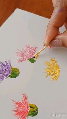 a person is drawing with colored pencils on paper and using a brush to draw the flowers