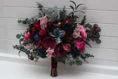 a bridal bouquet with red, purple and green flowers on a white wall background