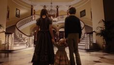 two people and a child are standing in front of the stairs at an elegant house