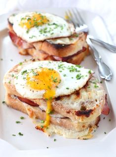 two sandwiches with eggs on them are sitting on a plate next to a fork and knife