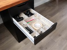 an open drawer with various items in it on a wooden floor next to a table