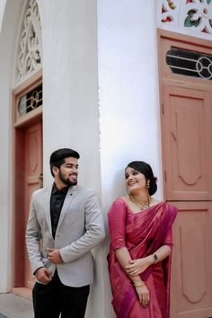 a man and woman standing next to each other in front of a building with pink doors