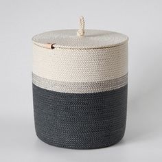 a black, white and grey basket with rope on the top is shown in front of a gray background