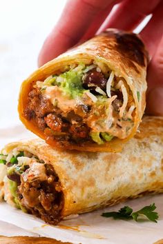 a hand holding a burrito filled with meat and veggies on top of it