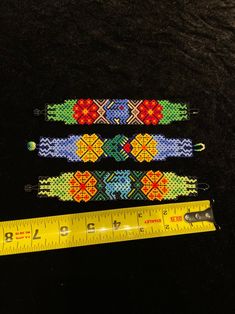 three colorful bracelets next to a measuring tape on a black surface with a ruler