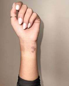 a woman's hand with a small heart tattoo on her left wrist and the other arm