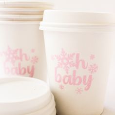 two white cups sitting next to each other with pink lettering on them and snowflakes