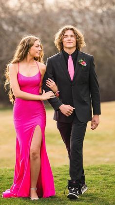 a man in a suit walking next to a woman in a pink dress on the grass