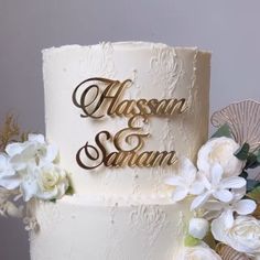 a wedding cake decorated with white flowers and gold lettering