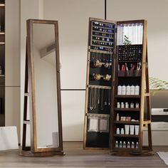 an open wooden jewelry cabinet sitting on top of a hard wood floor next to a mirror