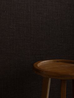 a wooden table with a vase on it next to a brown wall and black background