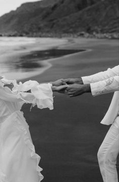 two people dressed in white dancing on the beach