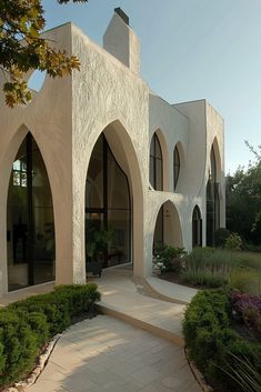 a white building with arched windows and plants in the front yard, on a sunny day