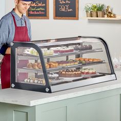 a man standing in front of a display case filled with cakes and pastries at a bakery