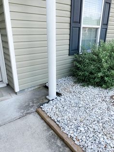 a house with gravel on the ground and bushes in front of it next to a door