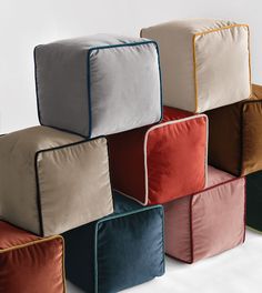 several different colored square pillows stacked on top of each other in front of a white wall