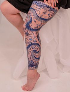 a woman is sitting down with her legs covered in blue and white tattoo designs on her leg