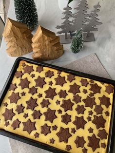 a cake with yellow icing and brown stars on it sitting in a pan next to christmas trees