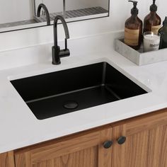 a black sink sitting under a bathroom mirror next to a counter top with soap dispensers