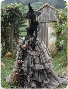 a woman in a black dress and hat with flowers on her head is standing outside