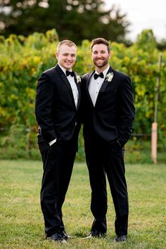 two men in tuxedos are posing for a photo together on the grass with trees in the background