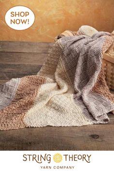 a knitted blanket sitting on top of a wooden floor next to a basket with yarn