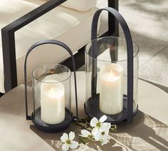 two white candles sitting on top of a table next to a vase filled with flowers