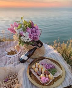 an outdoor table with flowers and food on it near the water's edge at sunset