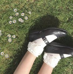 a woman's legs in white socks and black shoes on grass with daisies