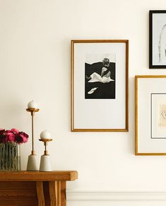 three framed pictures hang on the wall next to a table with vases and flowers