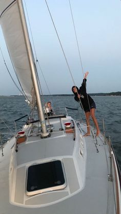 two people standing on the deck of a sailboat in the ocean with their arms up