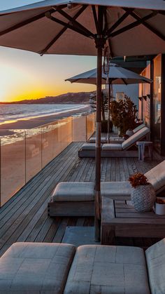 the sun is setting on an oceanfront deck with chaise lounges and umbrellas